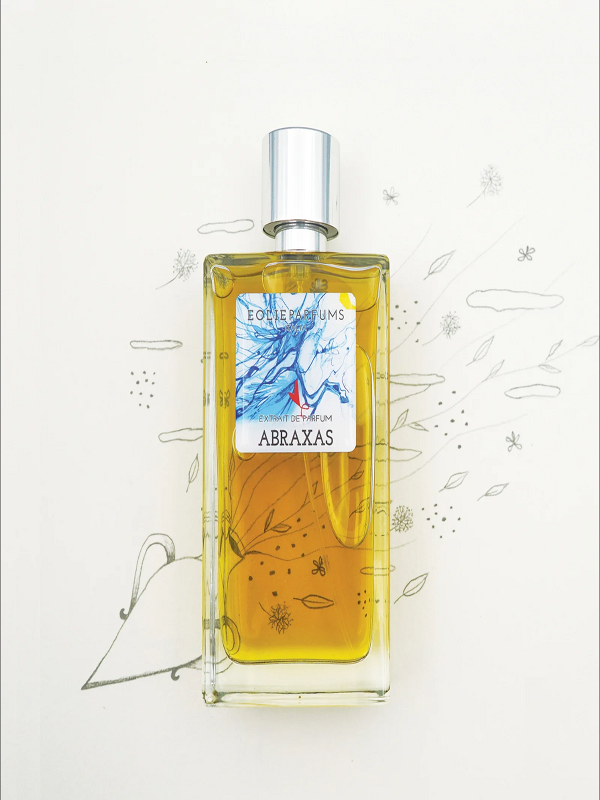 A rectangular glass perfume bottle filled with golden-yellow liquid, featuring a silver cap and a front label reading 'Etoiles Perles' and 'ABRAXAS'. The bottle is centered on a white background with delicate hand-drawn botanical sketches.