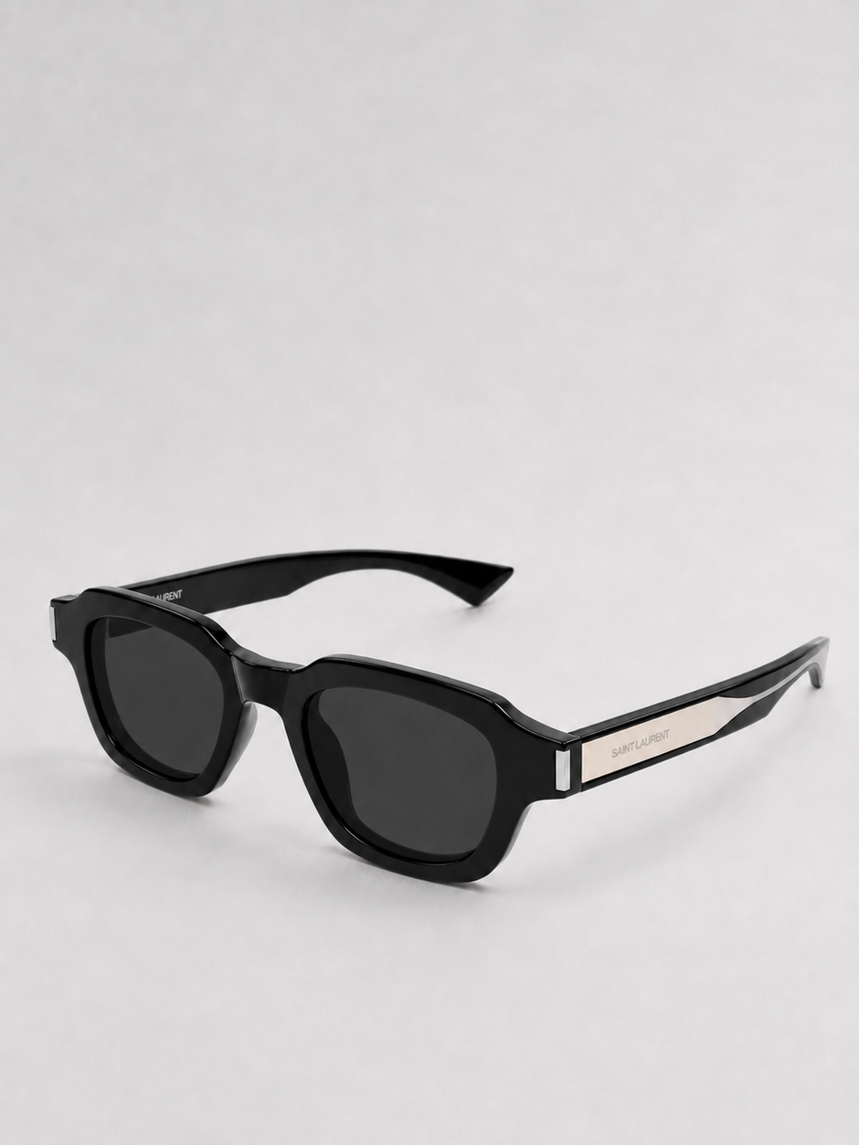 Black sunglasses with a thick geometric frame and dark lenses, featuring a silver-tone metal accent on the temple arm with the brand name
